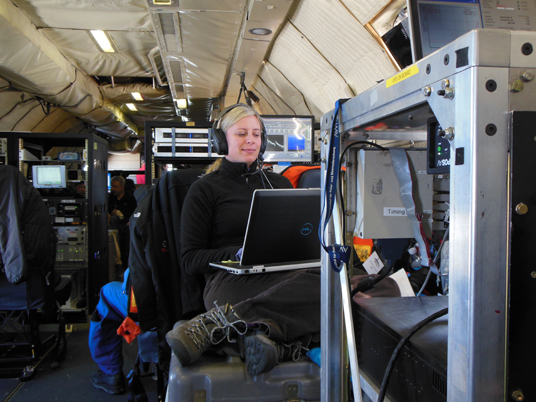 Christy sitting on a toolbox working on the plane during flight surrounded by various instrumentation. Credit: Christy Hansen