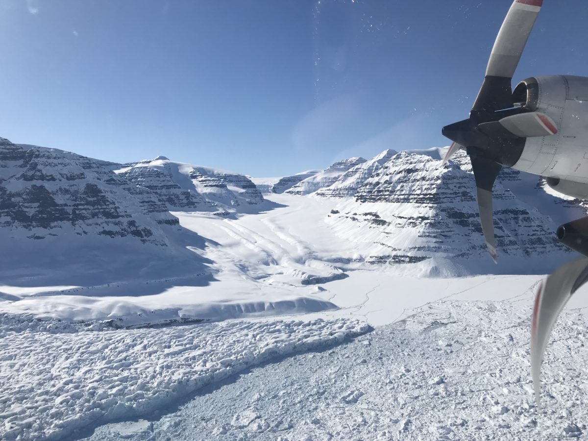 Photo showing land ice in the bottom left corner flowing down through a channel in the center. Sea ice is shown in the bottom right corner.